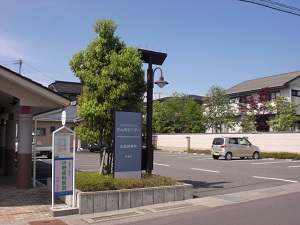 道路に面した敷地内に一本の木や街灯と看板が立ち、傍にバス停が設置されている写真