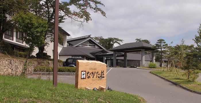 駐車場から入口までが緩やかな坂になっており白を基調とした和風な造りのながた荘(公共の宿)の外観写真