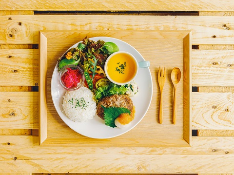 木のトレーに白い丸いお皿が置かれスープやごはん、野菜サラダ、肉料理が盛られている写真