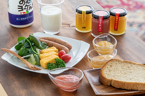 机上に飲むヨーグルト、ジャムの瓶が3本、パンや白いお皿にソーセージ、卵焼き、野菜サラダが盛られた写真