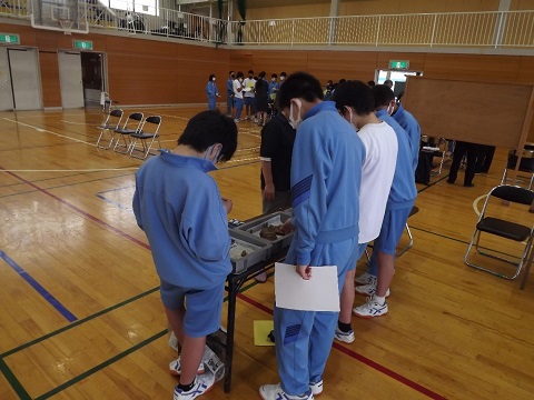 土器の欠片が入ったケースが置かれた長机の周りに5名の生徒が集まり、担当者と土器の接合を行っている様子の写真