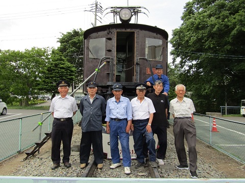 屋外に展示されている電気機関車ED19-1の前で、6名の機関車保存会の皆さんが並んでいる写真