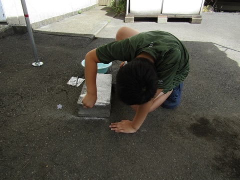緑色のシャツを着た男の子がブロックの角を使って高麗石を削っている様子の写真