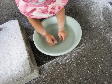 ピンク色の帽子を被った子供が、水が入った洗面器の中に手を入れて削った高麗石をピカピカにしている様子の写真