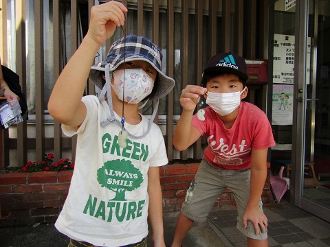 チェック柄の帽子と黒色のキャップを被った2名の子供が、完成した勾玉をカメラに見せている写真