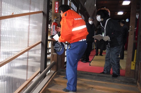 松島神社の建物内に設置された消火器を、オレンジ色の防寒着を着た消防署の担当者と女性スタッフが確認作業を行っている様子の写真