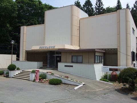 赤色のポストが設置された左に6段の階段と右にスロープが設置されたオフホワイト色の外壁の箕輪町郷土博物館の建物外観の写真