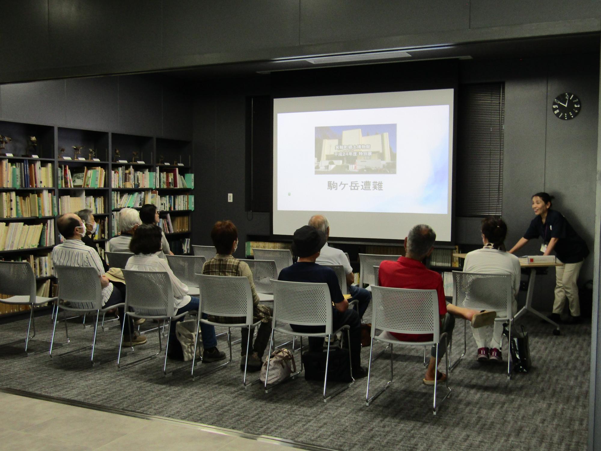 博物館の図書講座室でスクリーンに映った映像をみる参加者