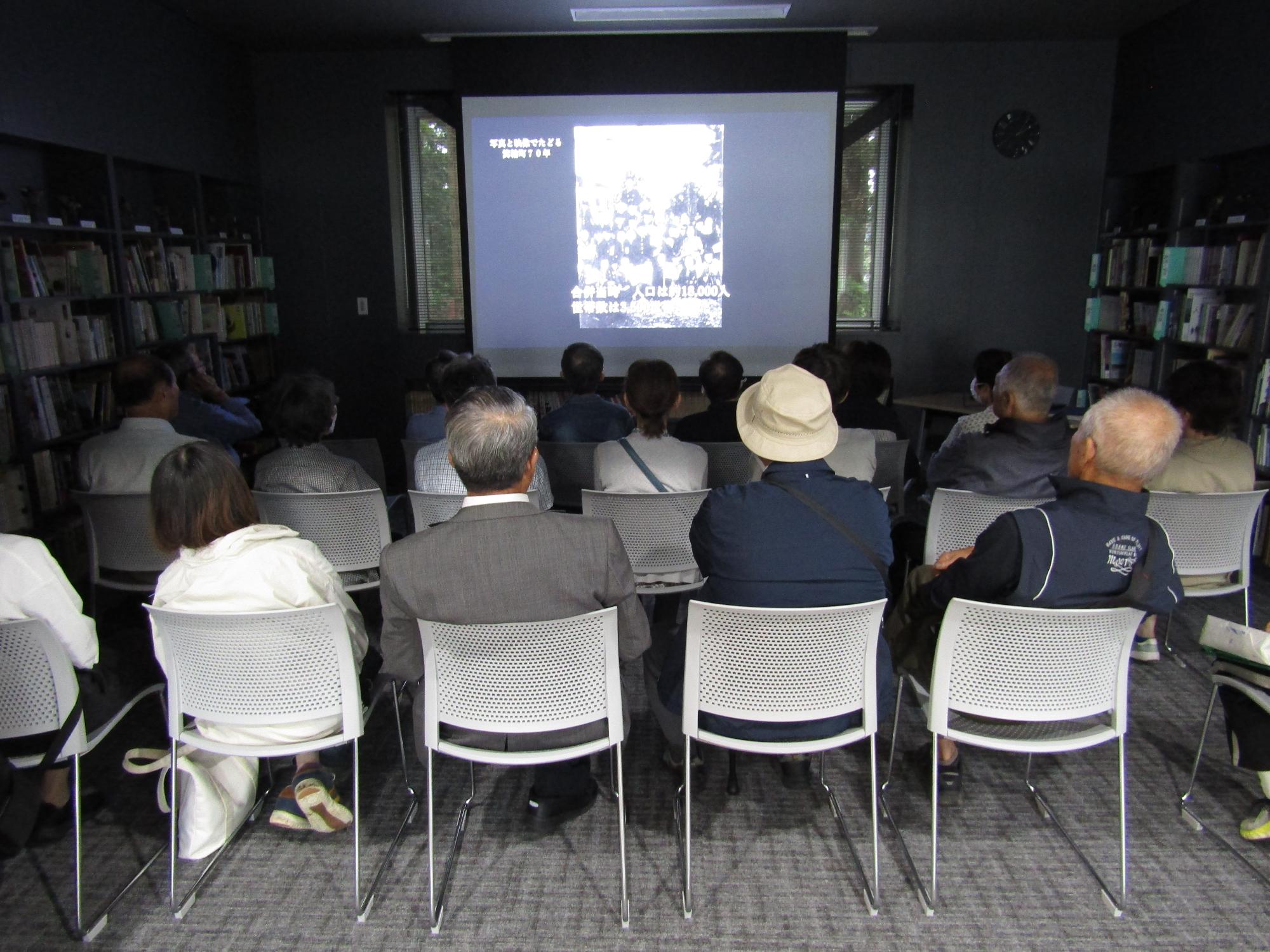 博物館の図書講座室で、椅子に座って映像を見る参加者