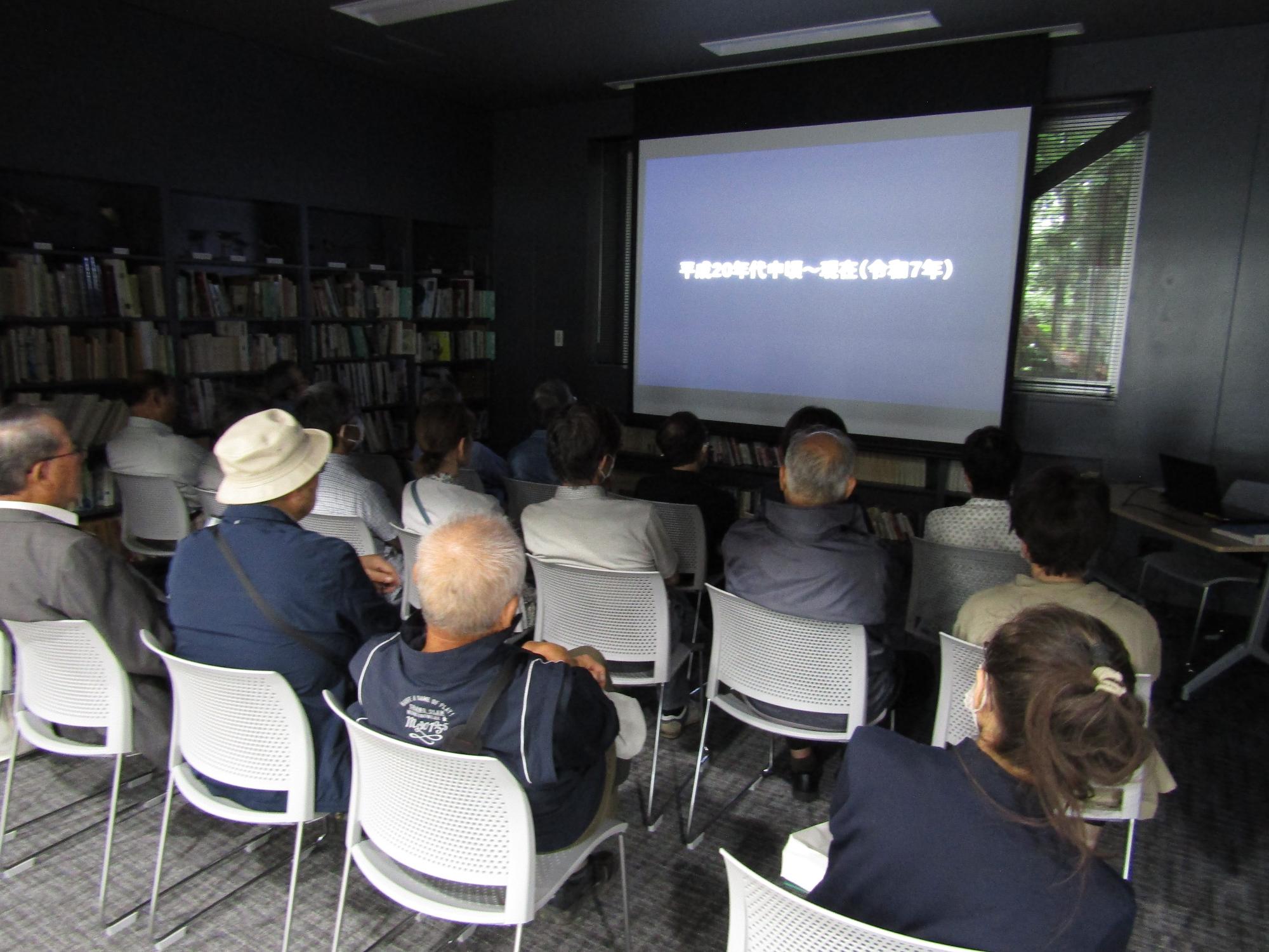 図書講座室で椅子に座って映像を見る参加者(南側から)