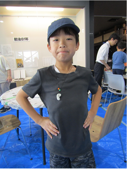 完成したまが玉のネックレスを首からかけてポーズをとる男の子