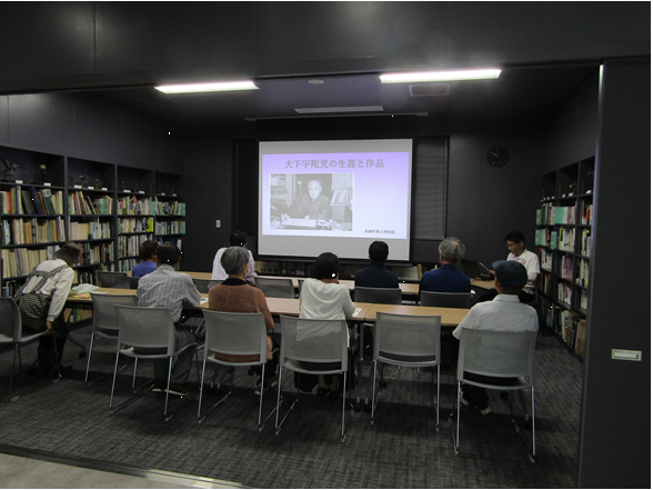 図書講座室で椅子に座りスクリーンを見ながら、話を聞く参加者の皆さん