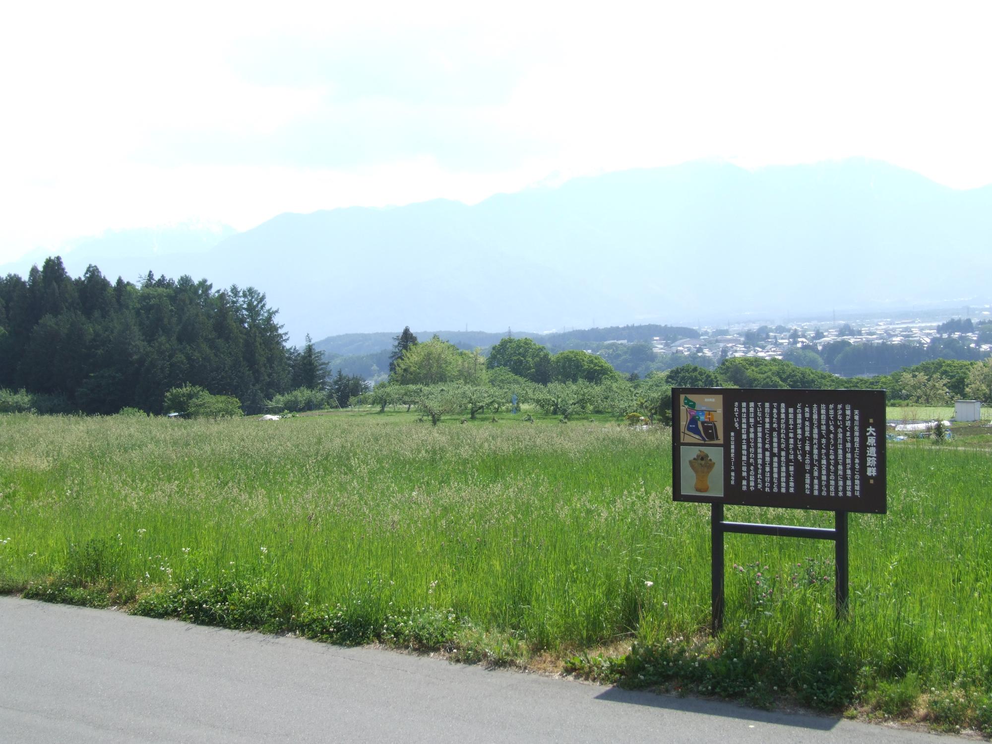 段丘上の平面に広がる福与大原遺跡。道路沿いに遺跡の存在を示す看板が立ち、奥には伊那谷を望む