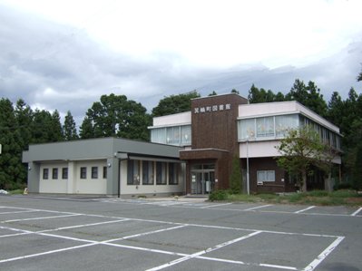 周囲を木々に囲まれ、広々とした駐車場が完備されている場所に、2階建ての高い位置に「箕輪町図書館」と書かれた建物外観の写真