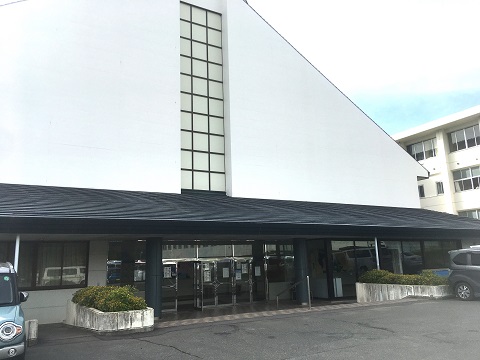 白壁の大きな三角屋根の中央に黒色の庇と柱が施された箕輪町社会体育館の入り口の写真