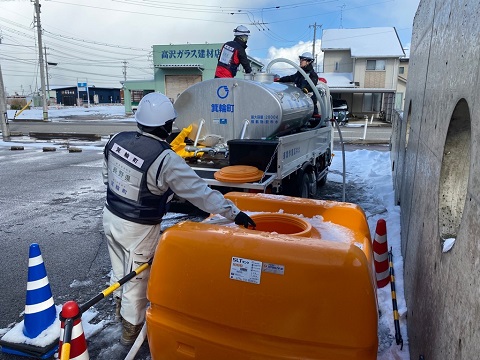 給水車から大きなオレンジ色のタンクへ給水が行われている写真