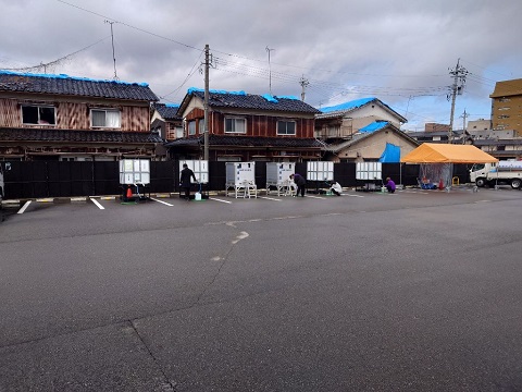 広い駐車場の壁側に6つの大きな四角いタンクが等間隔に置かれている給水拠点の写真
