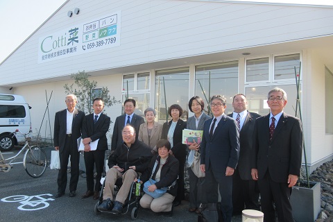 白壁の建物の前で、前列に女性と車いすに座った男性が座り、後列に9名の議員の方々が並んで立っている集合写真