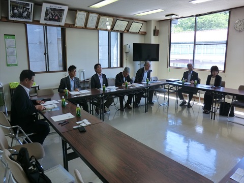 ロの字に設置された長机の席に議員の方々や関係者が座り話を聞いている視察研修の様子の写真