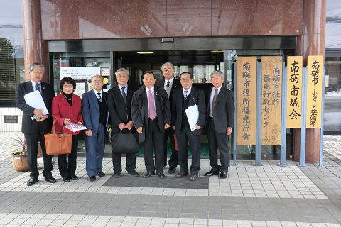南砺市議会の建物入り口に8人の関係者が並んでいる写真