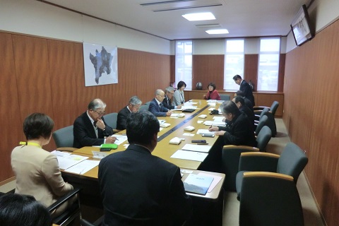 大きな机が置かれた会議室で約10名の関係者が会議をしている様子の写真
