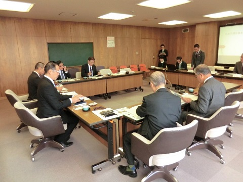 ロの字に設置された長机の席に議員の方々や関係者が座り、右側中央の席から立ち上がった男性の話を聞いている視察研修の様子の写真
