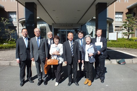 縦長の軒先の左右に角形の柱が立つ建物の前で、8名の議員の方々が並んでいる写真