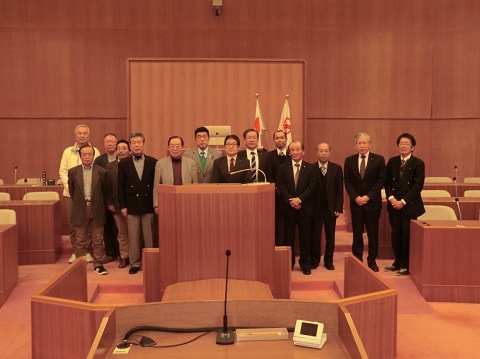 議会室内で14名の議員の方々が並んでいる記念写真