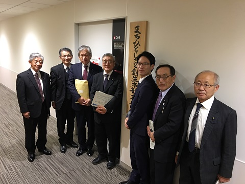内閣官房 まち・ひと・しごと創成本部事務局の部屋の前に立つ7人のスーツ姿の男性の写真