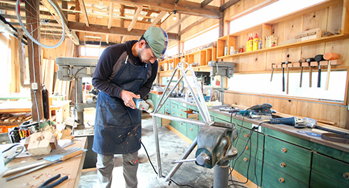 様々な工具や機械が置かれた作業場で自転車のフレームを作成している安田さんの写真