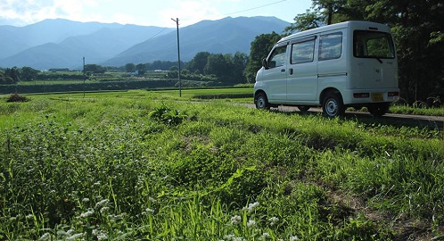 畑の間の農道を走る一台の白い車の写真
