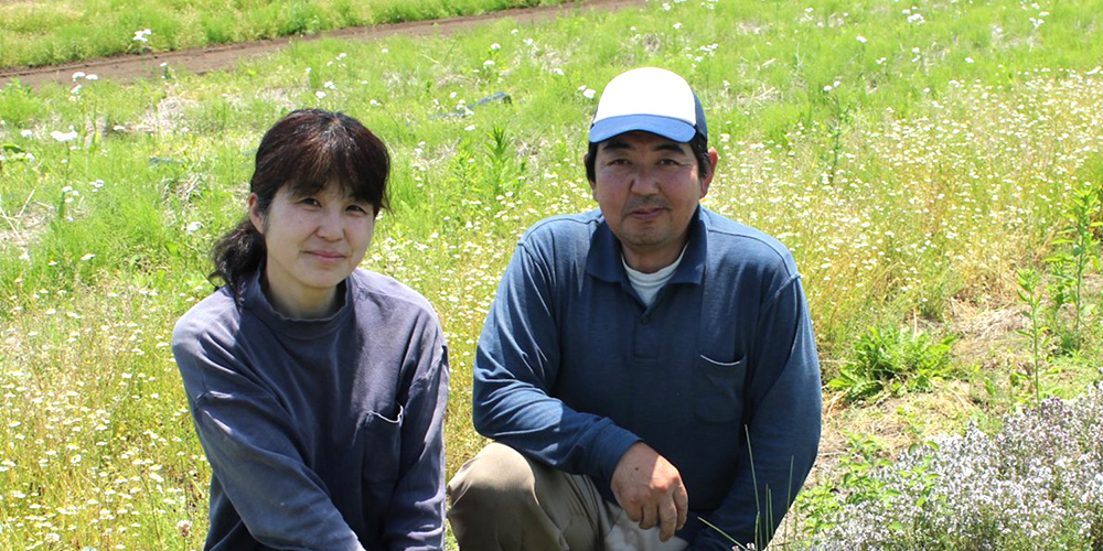 花が咲いている屋外で座っている長谷川さんと奥様の写真