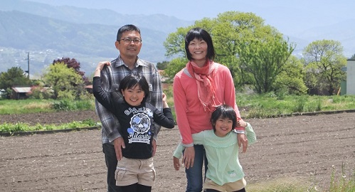 畑の前に立っているお父さん、お母さん、二人の子供の写真