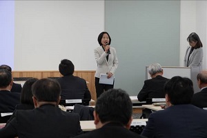 白いジャケットを着た女性が参加者達の前に立ち、マイクを持って話をしている写真