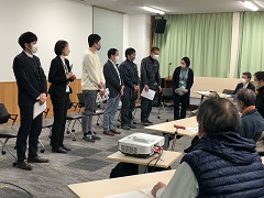 室内前方で7名の方が横一列になって並び、席についている参加者達の方を向いている写真