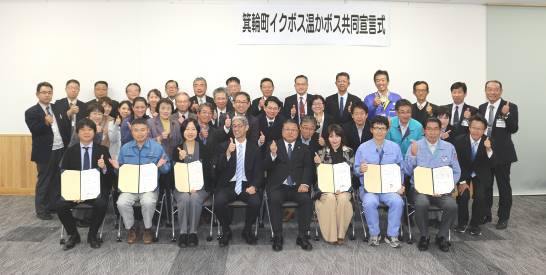 「箕輪町イクボス温かボス共同宣言式」と書かれた横断幕が貼られた壁をバックに、参加者達が集まり記念撮影をしている写真