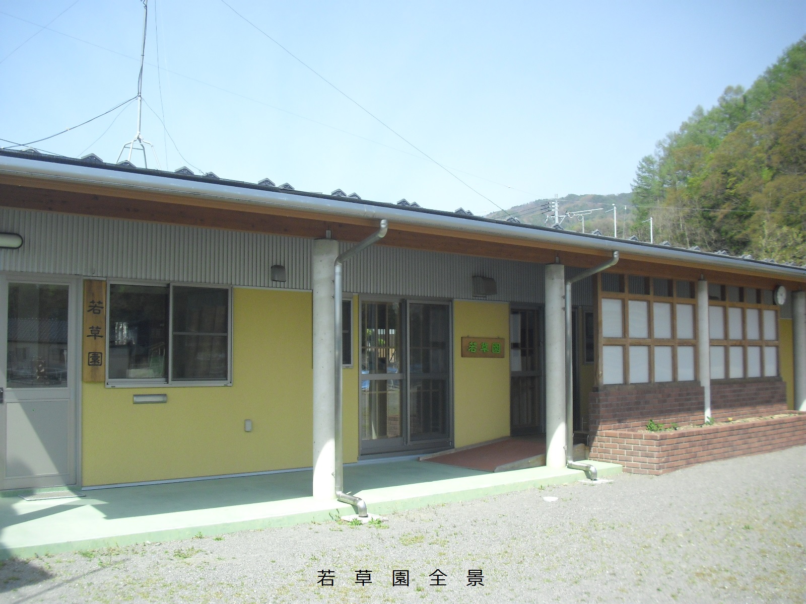 一部が黄色い壁で、木の板に「若草園」と書かれた看板が壁に掲げられている1階建てで横長の若草園全景の写真