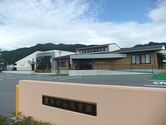 「東みのわ保育園」と書かれたベージュ色の門の奥に駐車場と園舎が見える東みのわ保育園を門側から撮影した写真