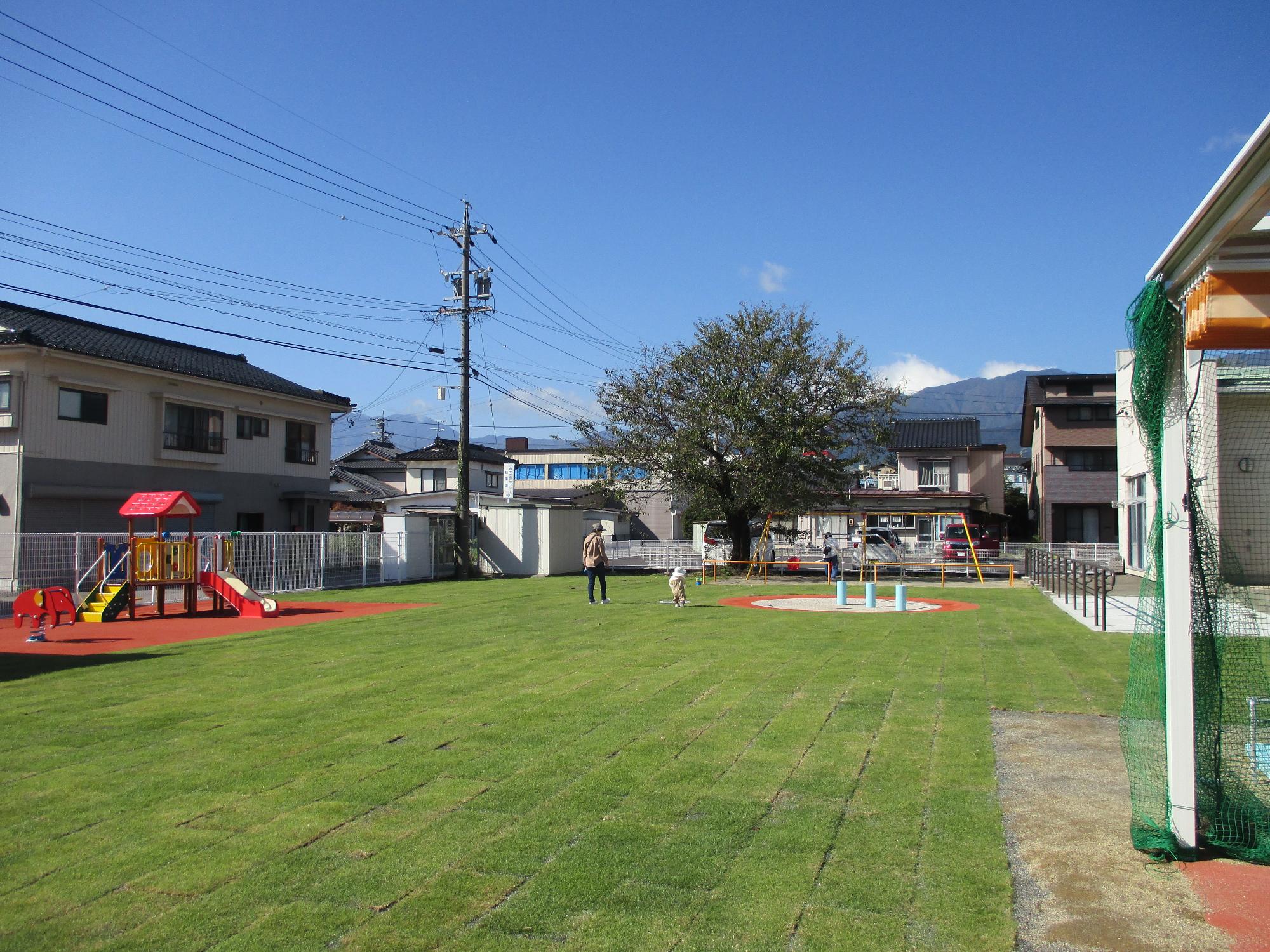 広い芝生の庭に複合遊具があり、遠くに親子2組