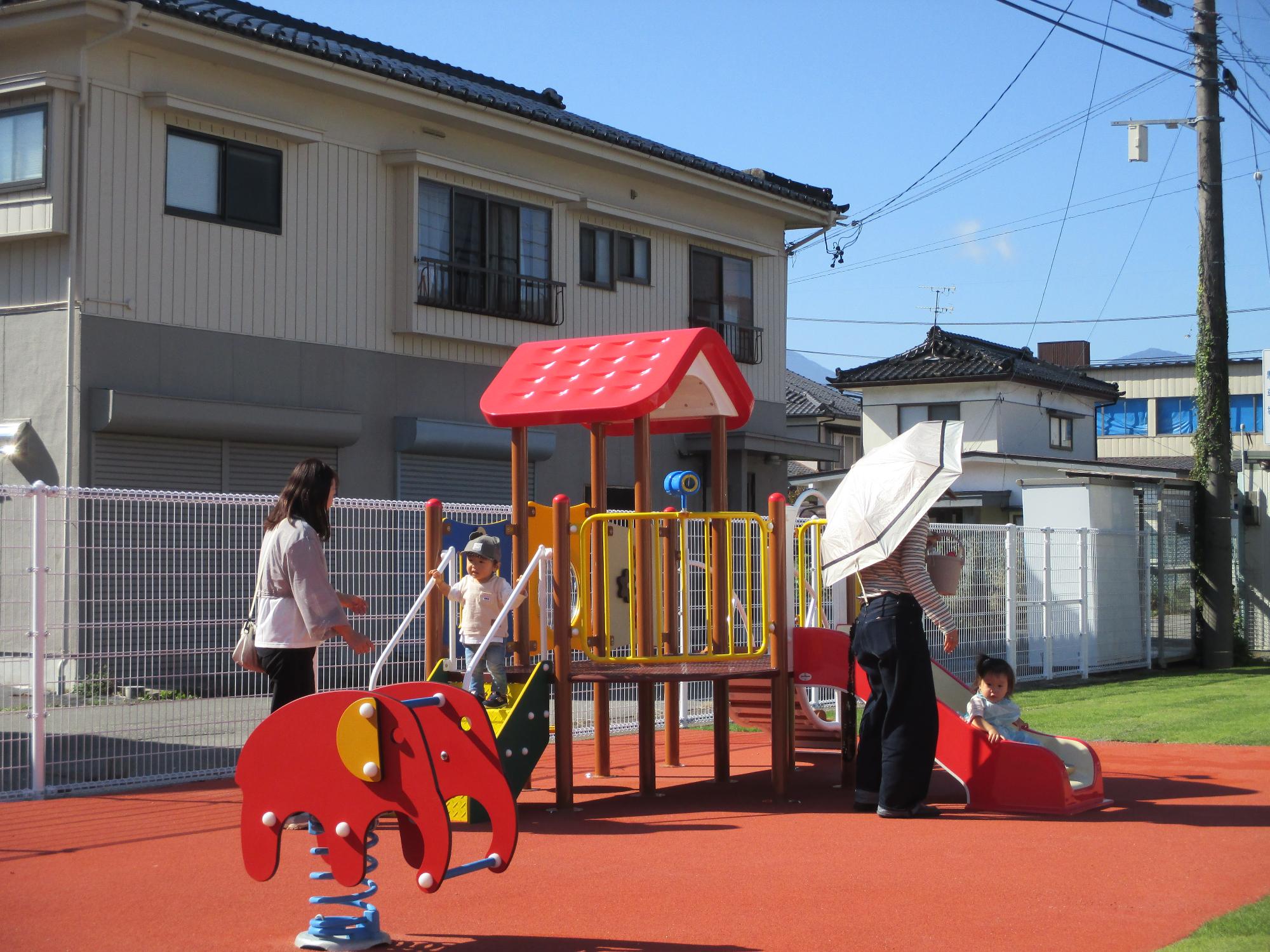 複合遊具であそぶ親子2組、手前にゾウのスプリング遊具