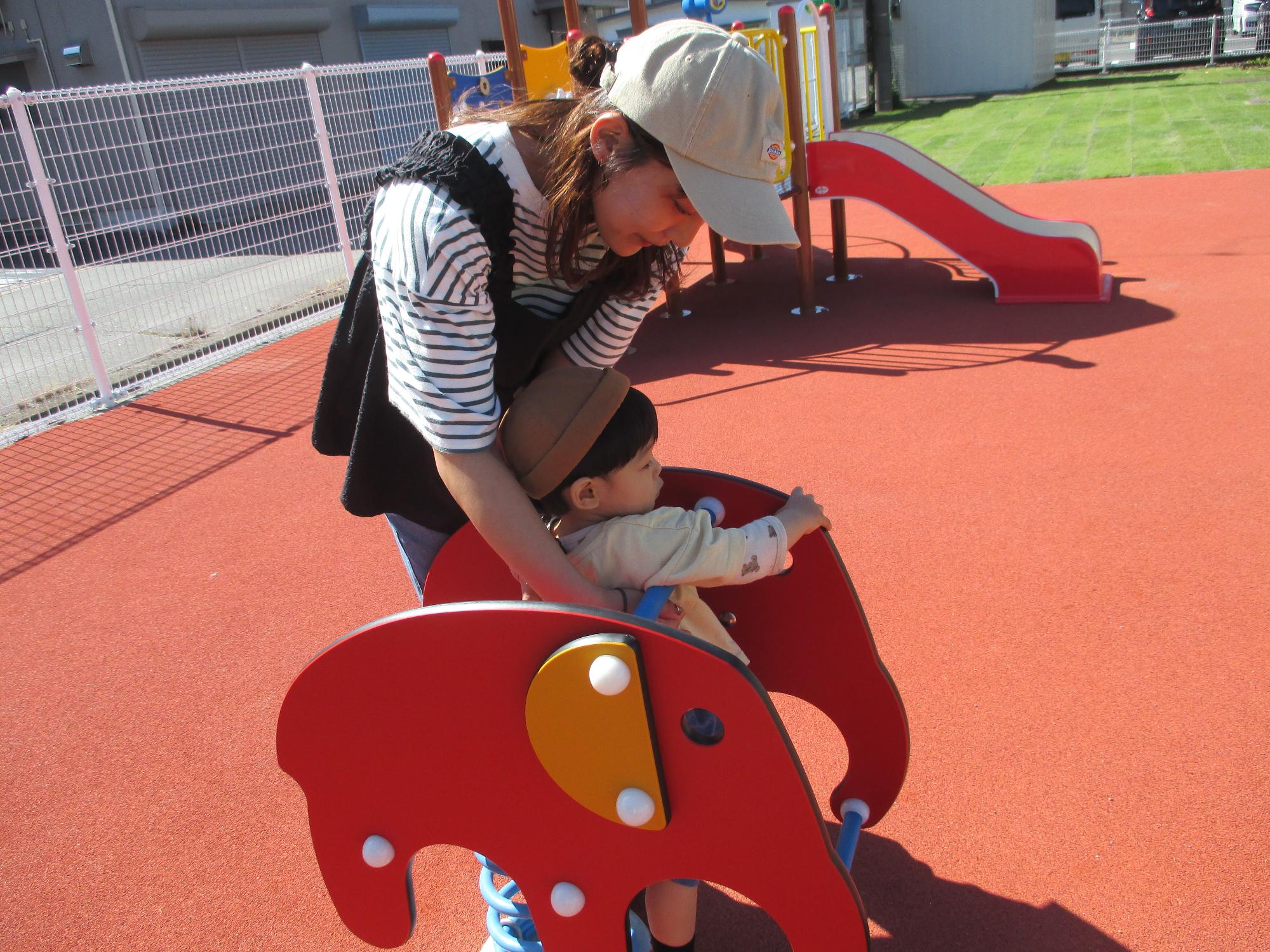 ゾウのスプリング遊具に子どもが乗れるよう手伝っている母