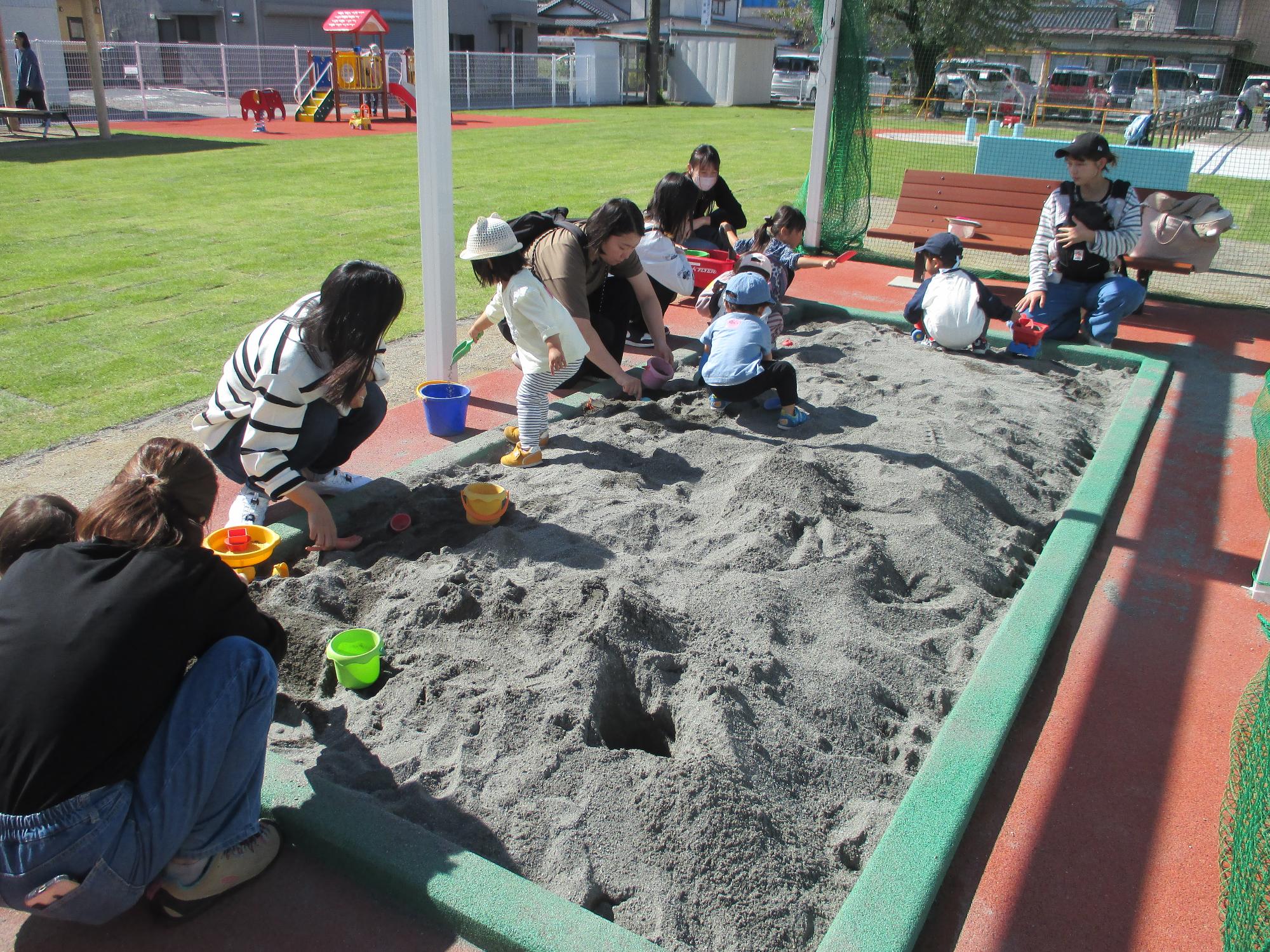 大勢の親子がしゃがんで砂あそび