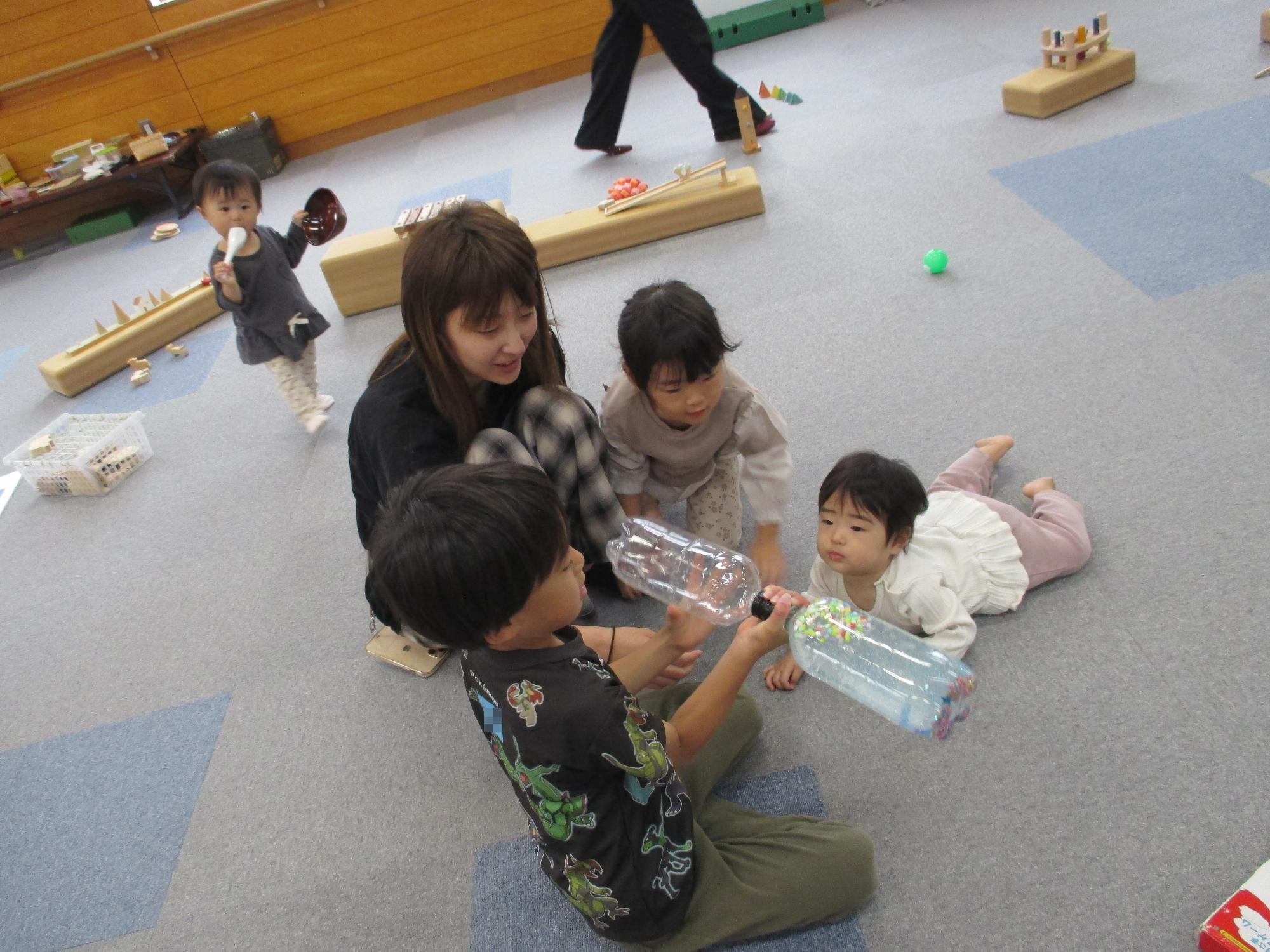 ペットボトルの手作りおもちゃをの持っている兄を見ている妹2人と母