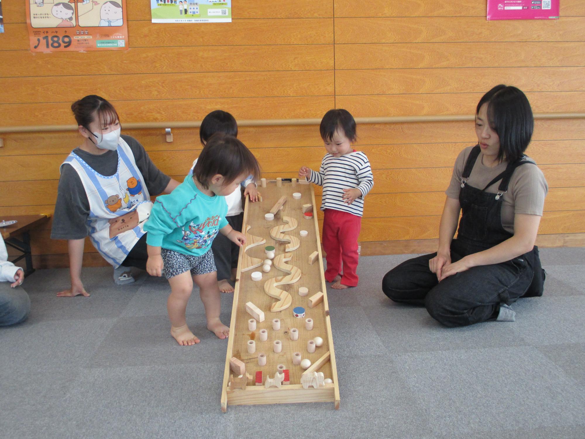 障害物がある坂道風おもちゃで木球が転がり落ちるところを見ている1歳児。