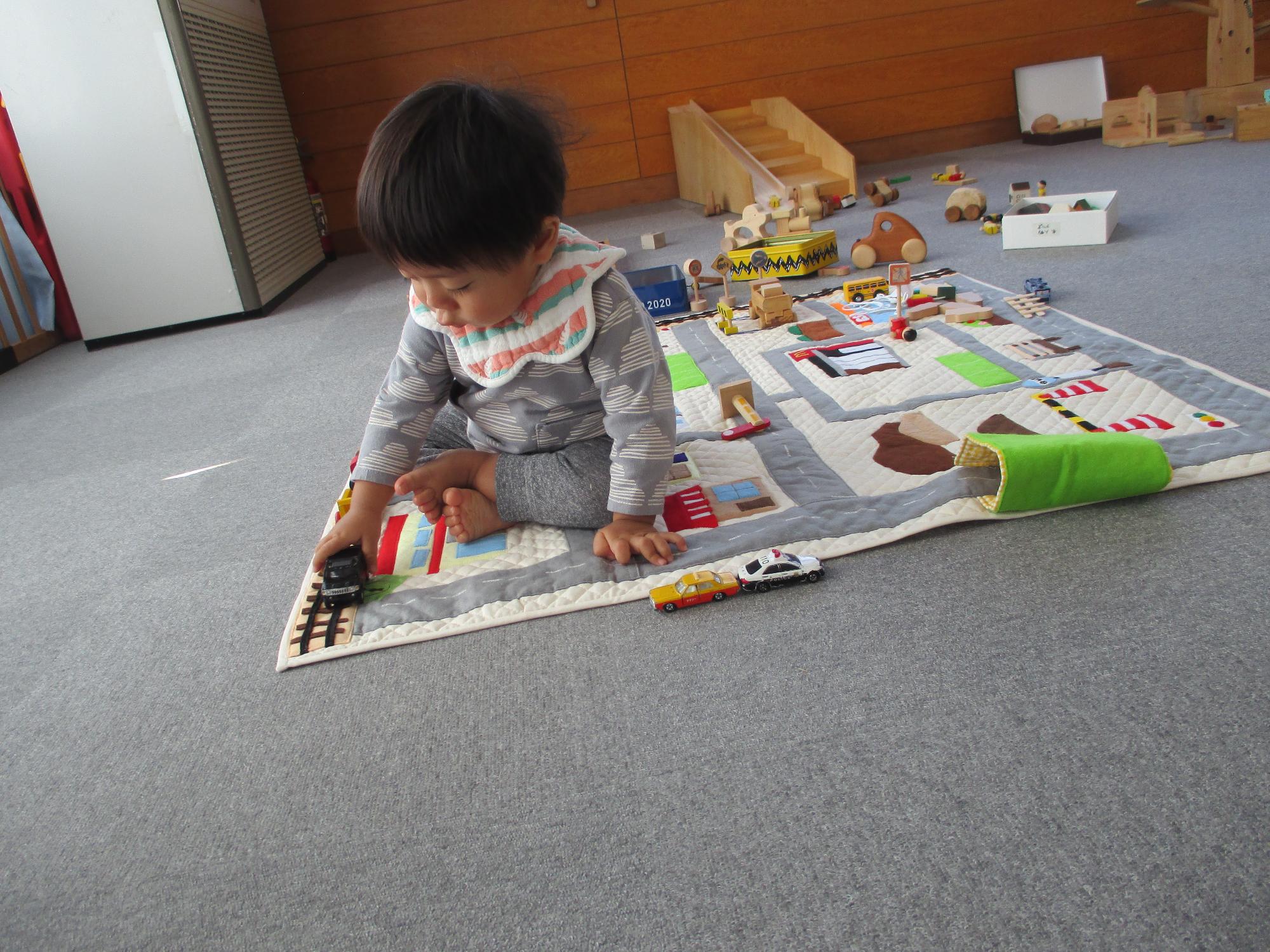 プレイマットの線路の上を汽車を走らせる1歳児