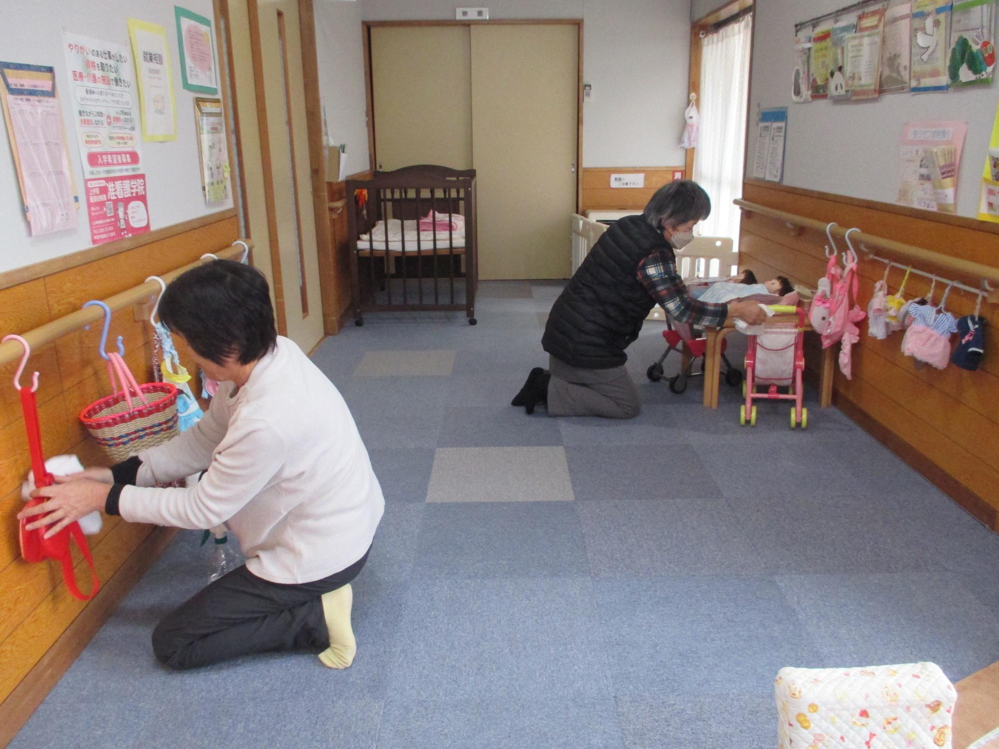 2人の女性が右壁と左壁に向かい壁沿いのおもちゃを拭いていている