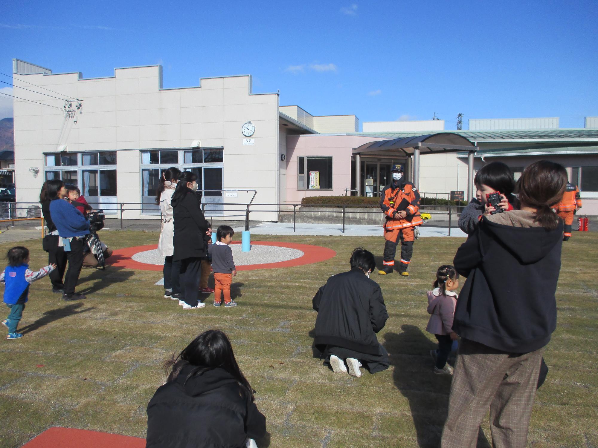 2子育て支援センターの庭で消防士の話を聞いている親子