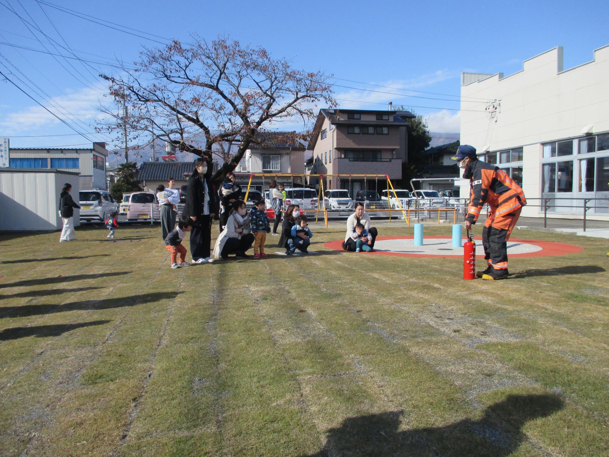 芝生の庭で消防士から消火器の使い方の説明を聞いている親子