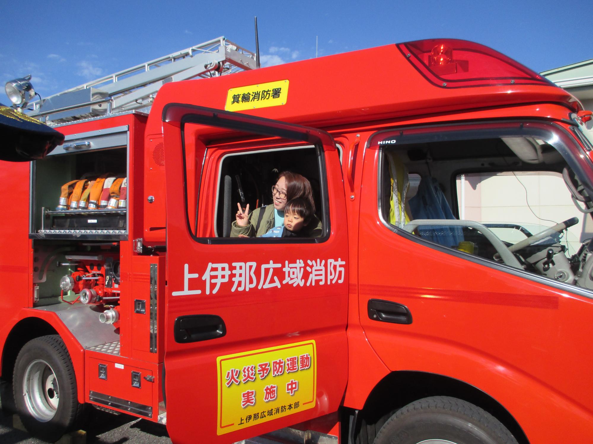 消防車両に乗ってピースサインをする母と子