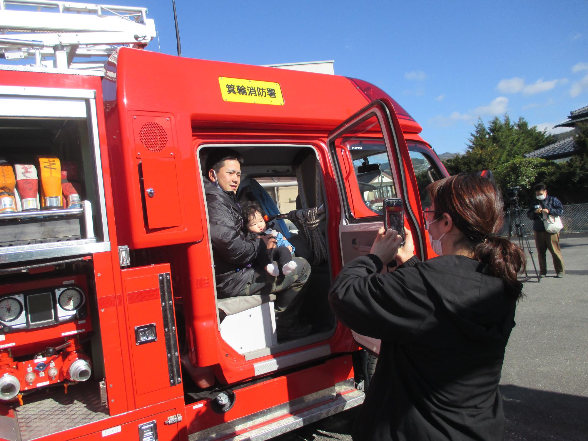 父子が消防車両に乗りその様子をスマホで撮っている母